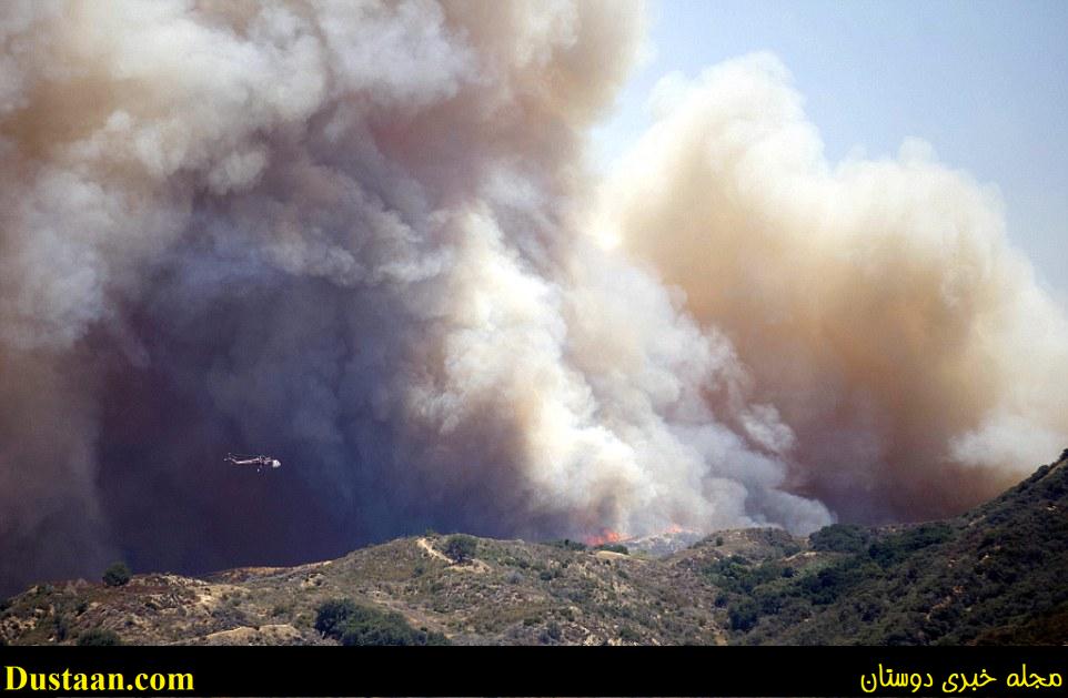 A helicopter is seen flying alongside the smoke as it drops retardant in a bid to control the flames  