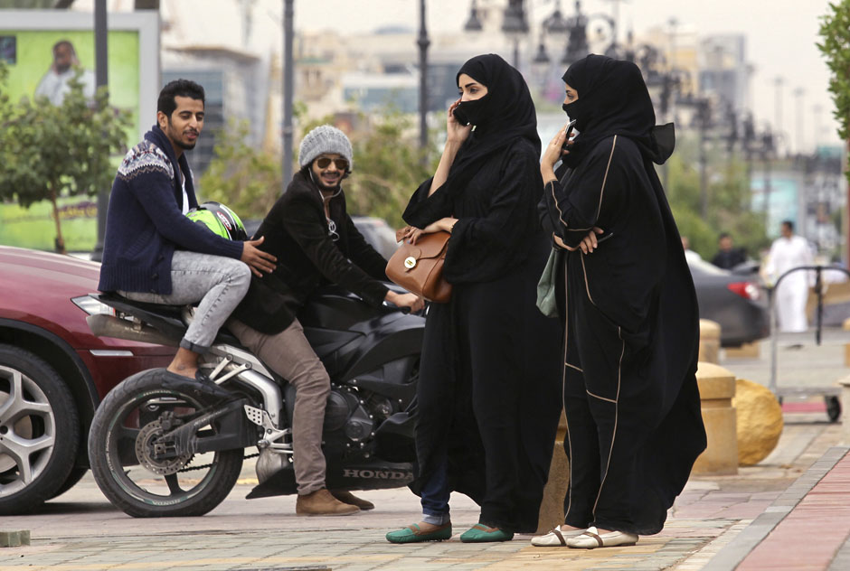 Woman speaks on the phone as men ride a motorcycle on a cloudy day in Riyadh